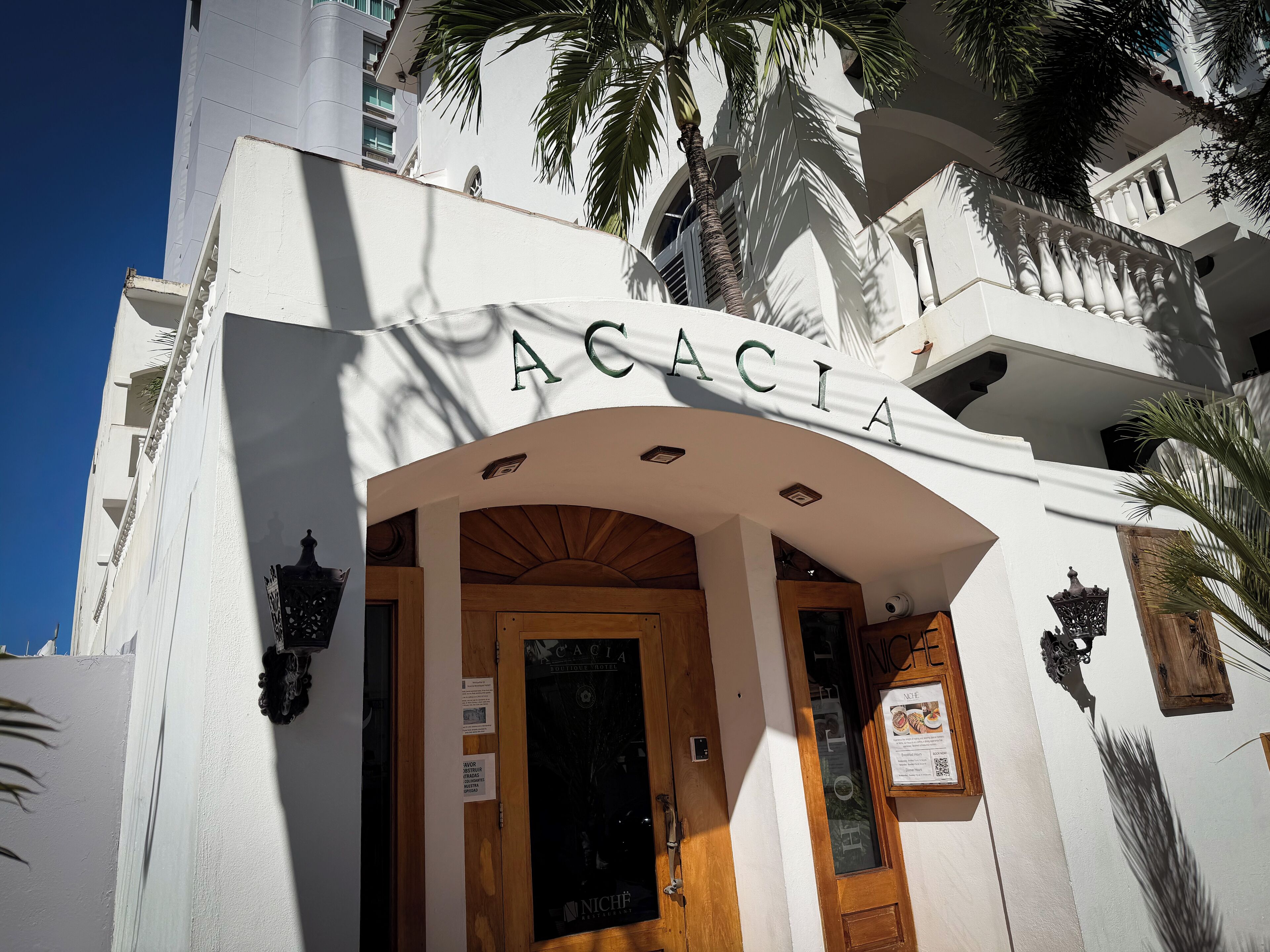 Exterior de l'Hotel Acacia Boutique, amb una entrada arqueada destacada, portes de fusta i un rètol sobre l'entrada.