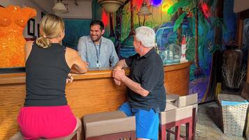 Una zona de bar con mostradores y taburetes de madera, un mural colorido en la pared y un gran jarrón decorativo.