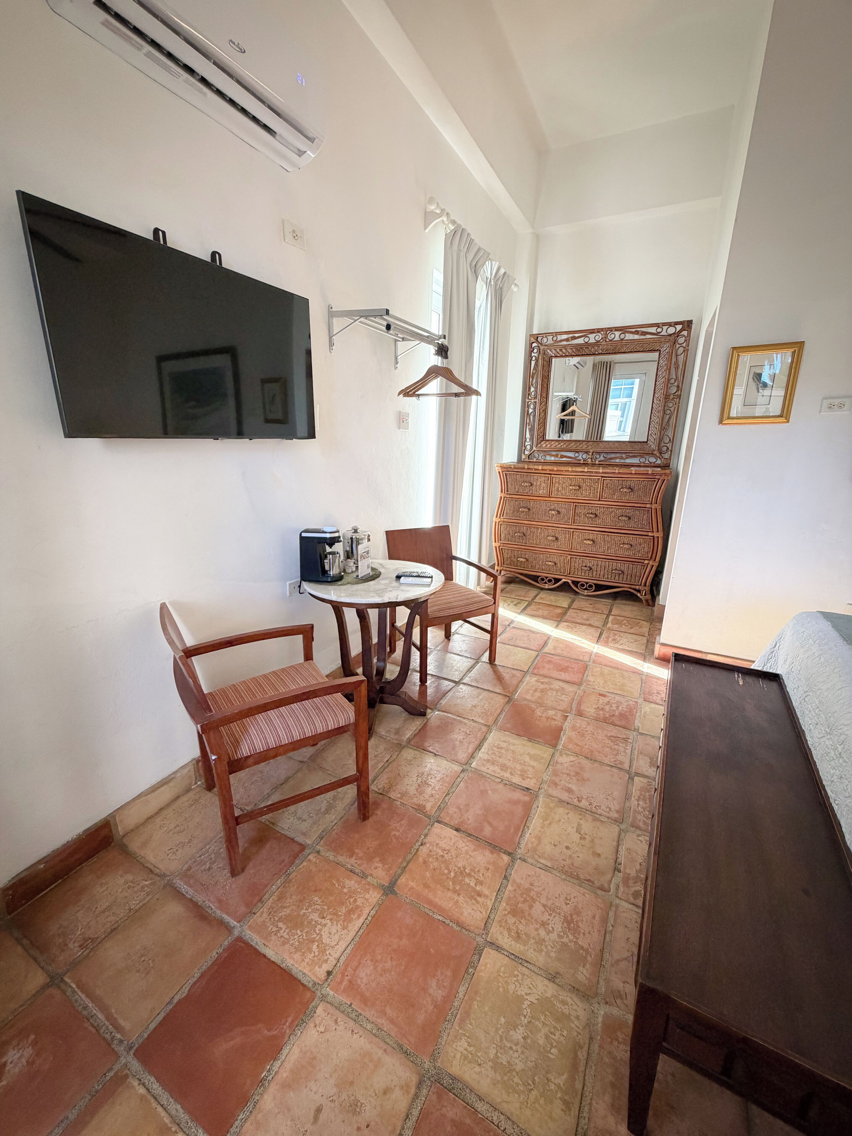 Une pièce avec un téléviseur fixé au mur, une table avec des chaises, une commode avec un miroir et un lit.