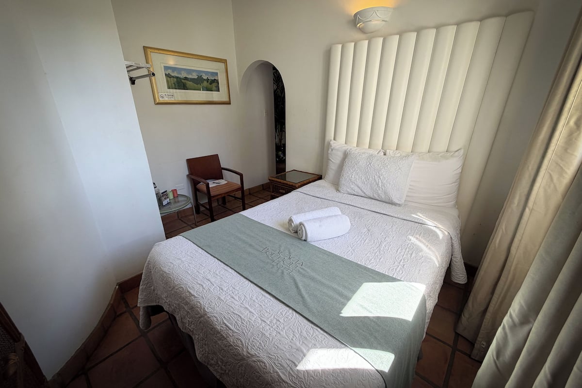Une chambre d’hôtel avec un lit, une chaise, une petite table et un tableau accroché au mur.