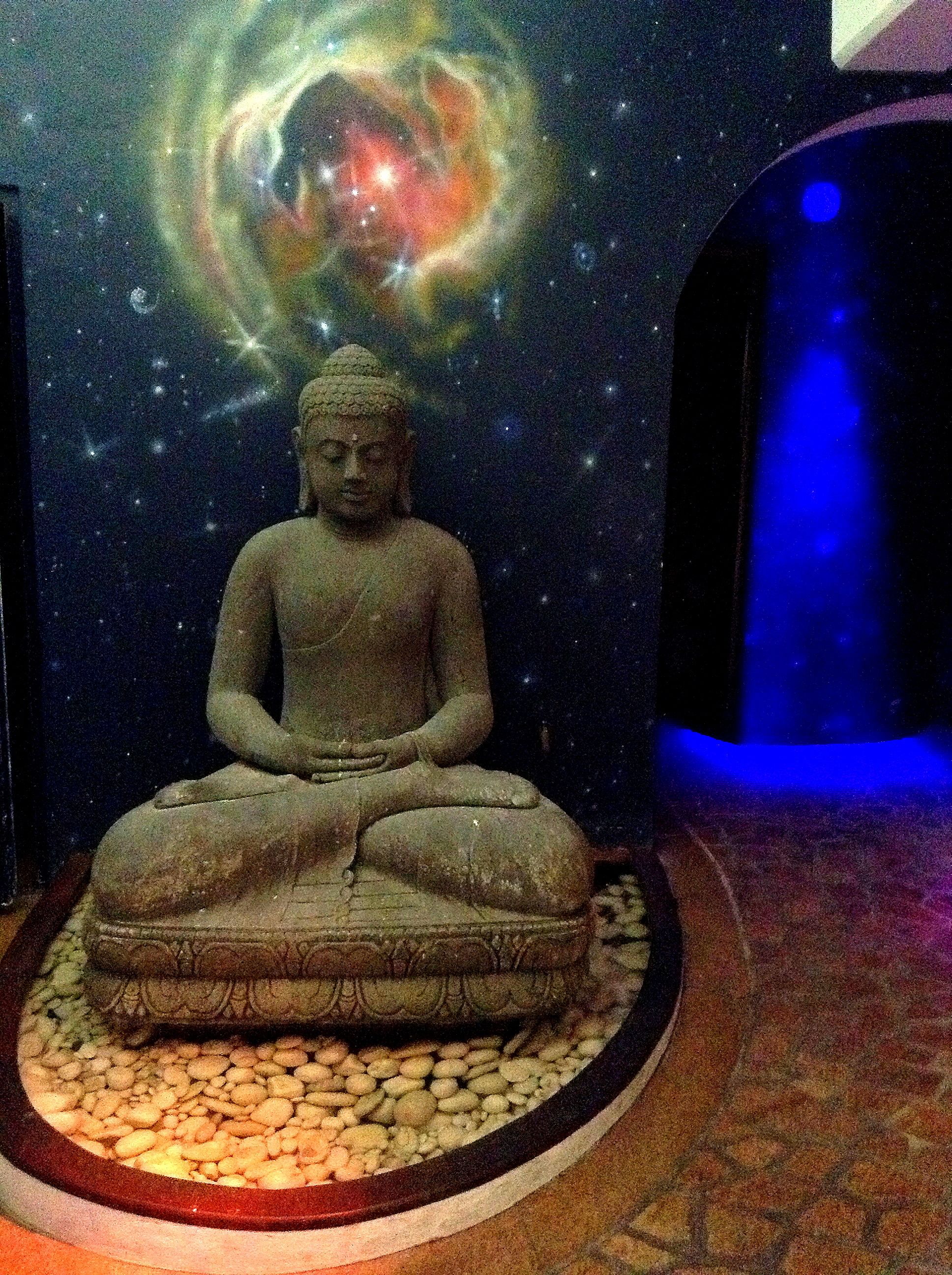Une statue de Bouddha en position méditative, entourée d’une fresque représentant un ciel étoilé.