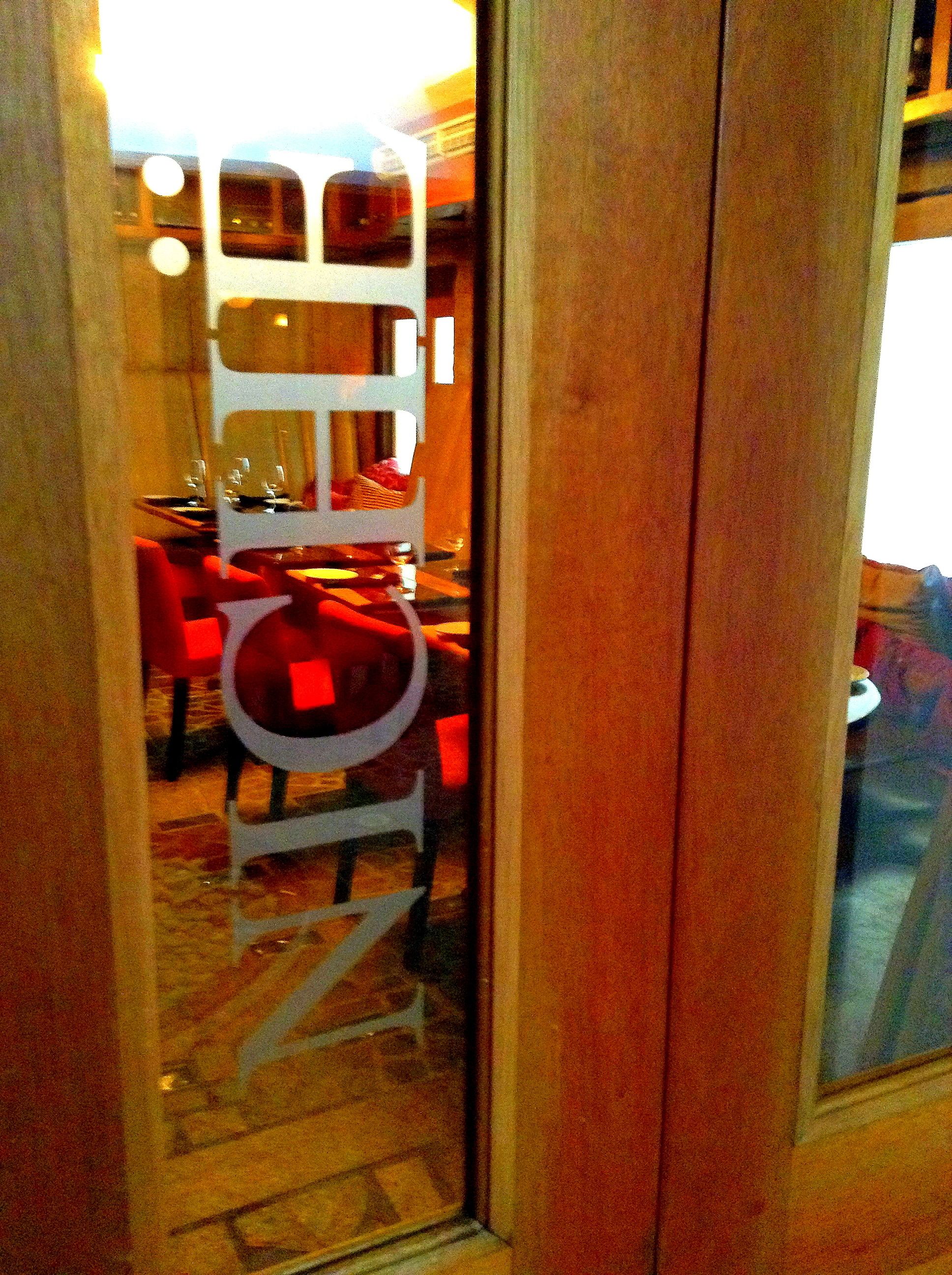 Vista a través de un ventanal hacia un comedor con sillas rojas y una mesa blanca.