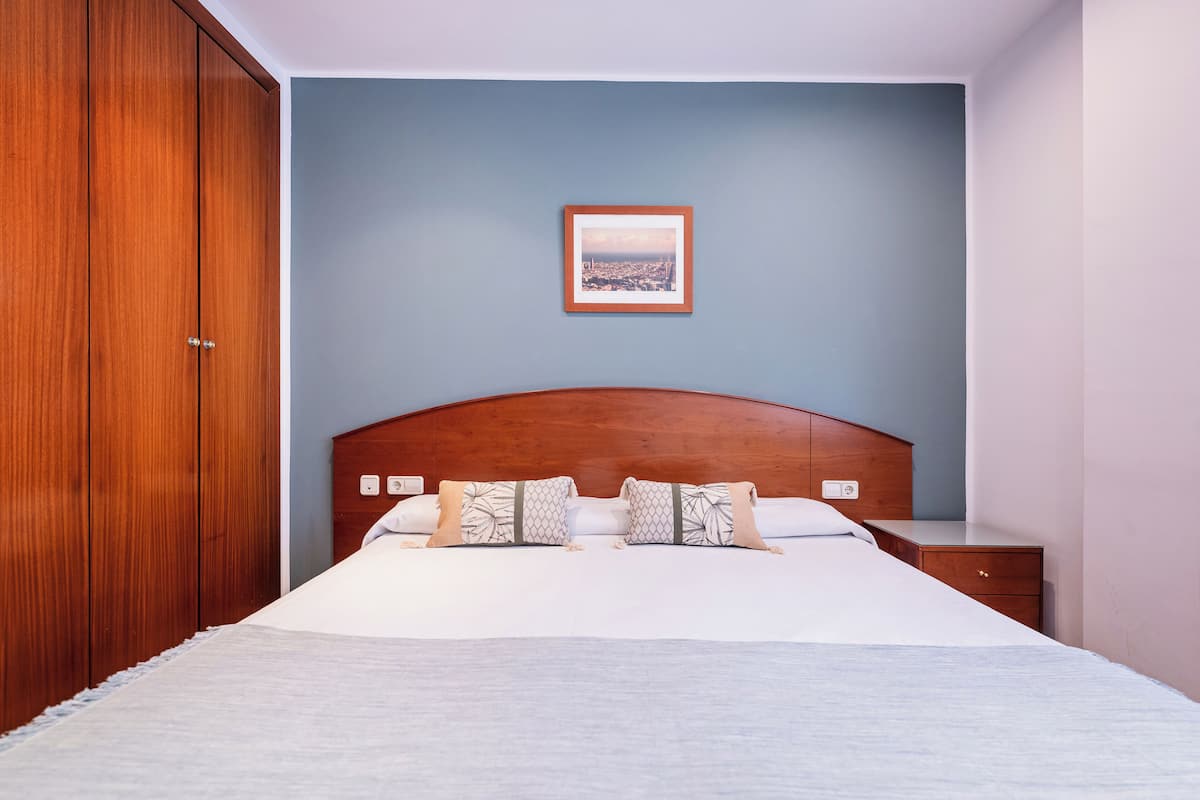 A bedroom with a wooden headboard, a bed with white bedding, two bedside tables, and a framed picture on the wall.