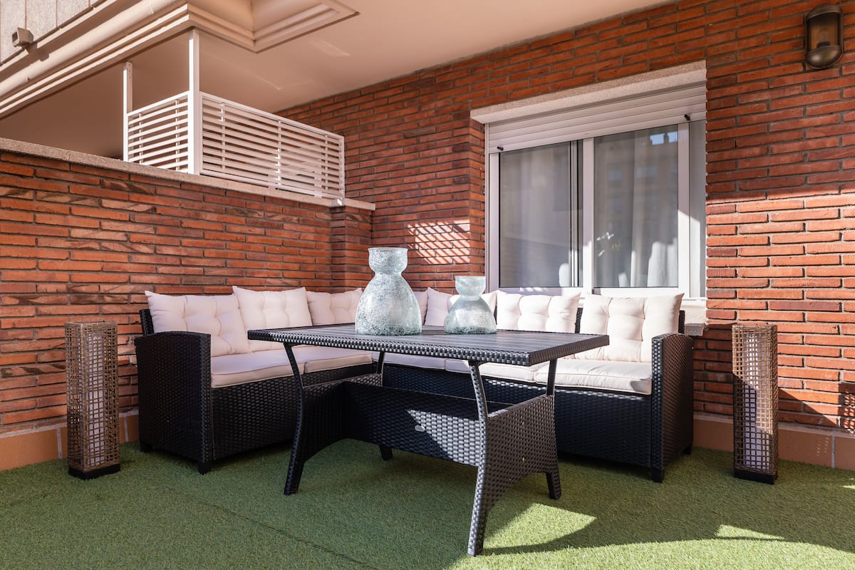 A patio with a wicker sofa, a table, and two tall vases.
