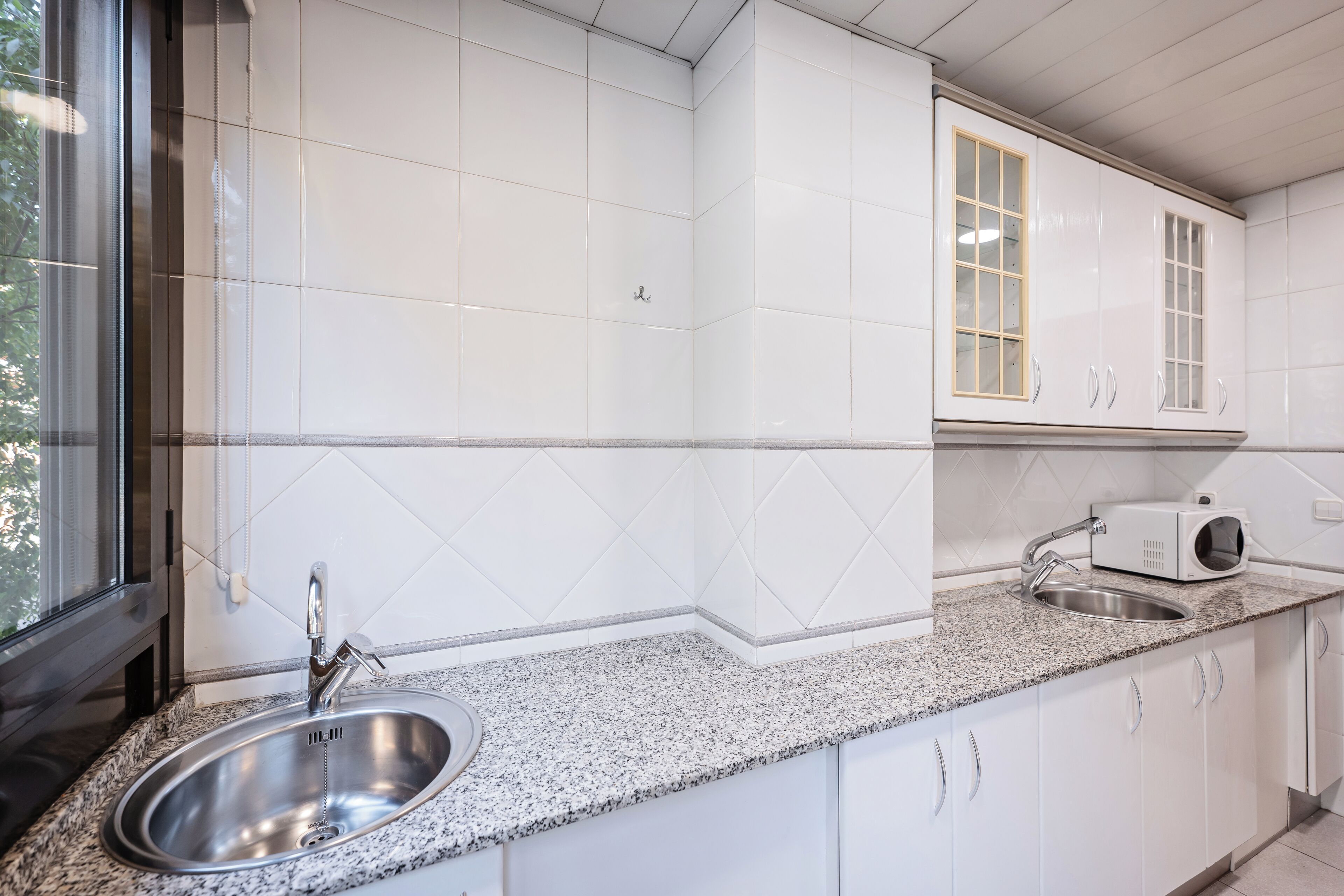 Una cocina con armarios blancos, encimera de granito, pileta de acero inoxidable y microondas.