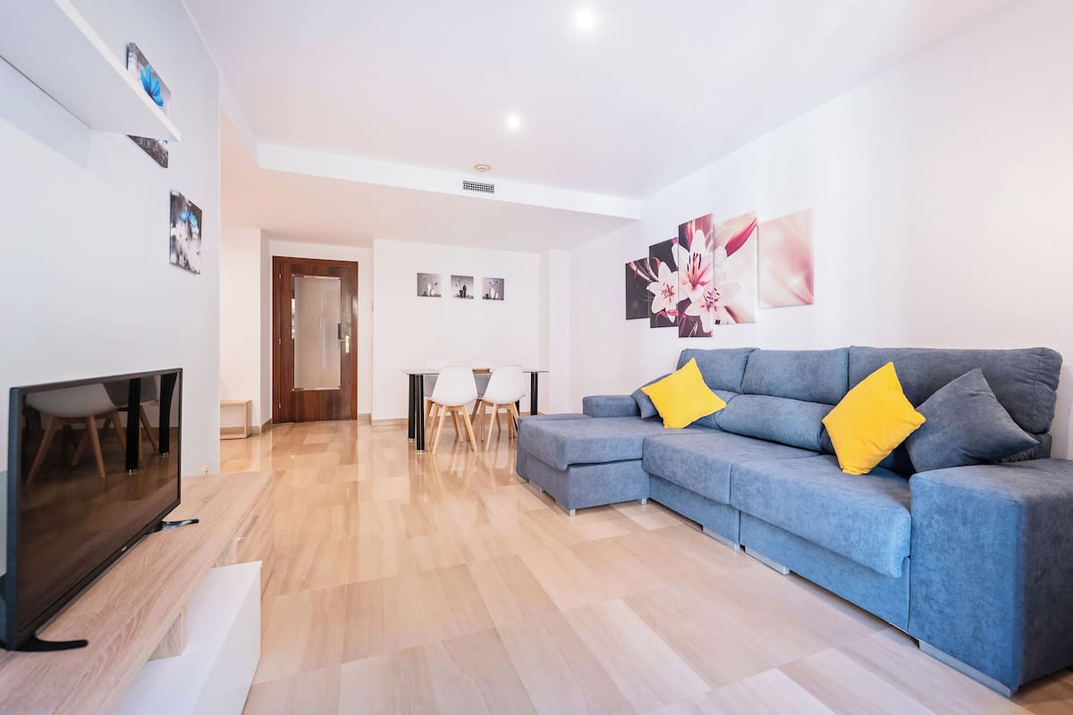 A modern living room with a grey sectional sofa, a flat-screen TV, and a dining area with a table and chairs.