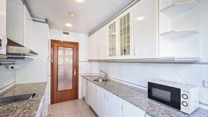 Una cocina con armarios blancos, encimera de granito, microondas y pileta de acero inoxidable.
