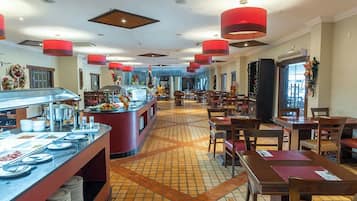 Espaço de refeições de hotel com buffet, várias mesas e cadeiras.
