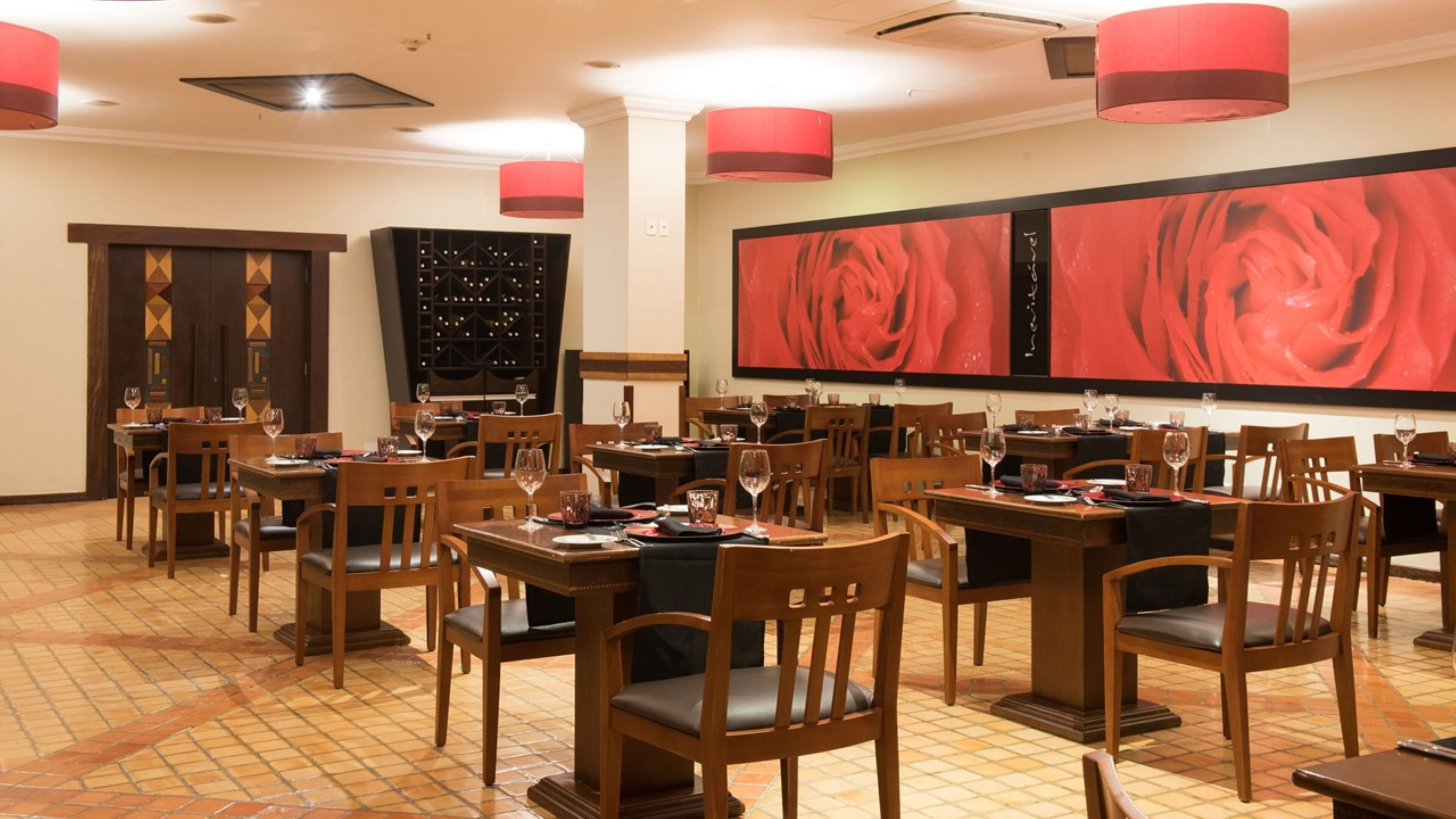 Un restaurante con varias mesas y sillas, un botellero y una obra de arte floral grande en rojo en la pared.
