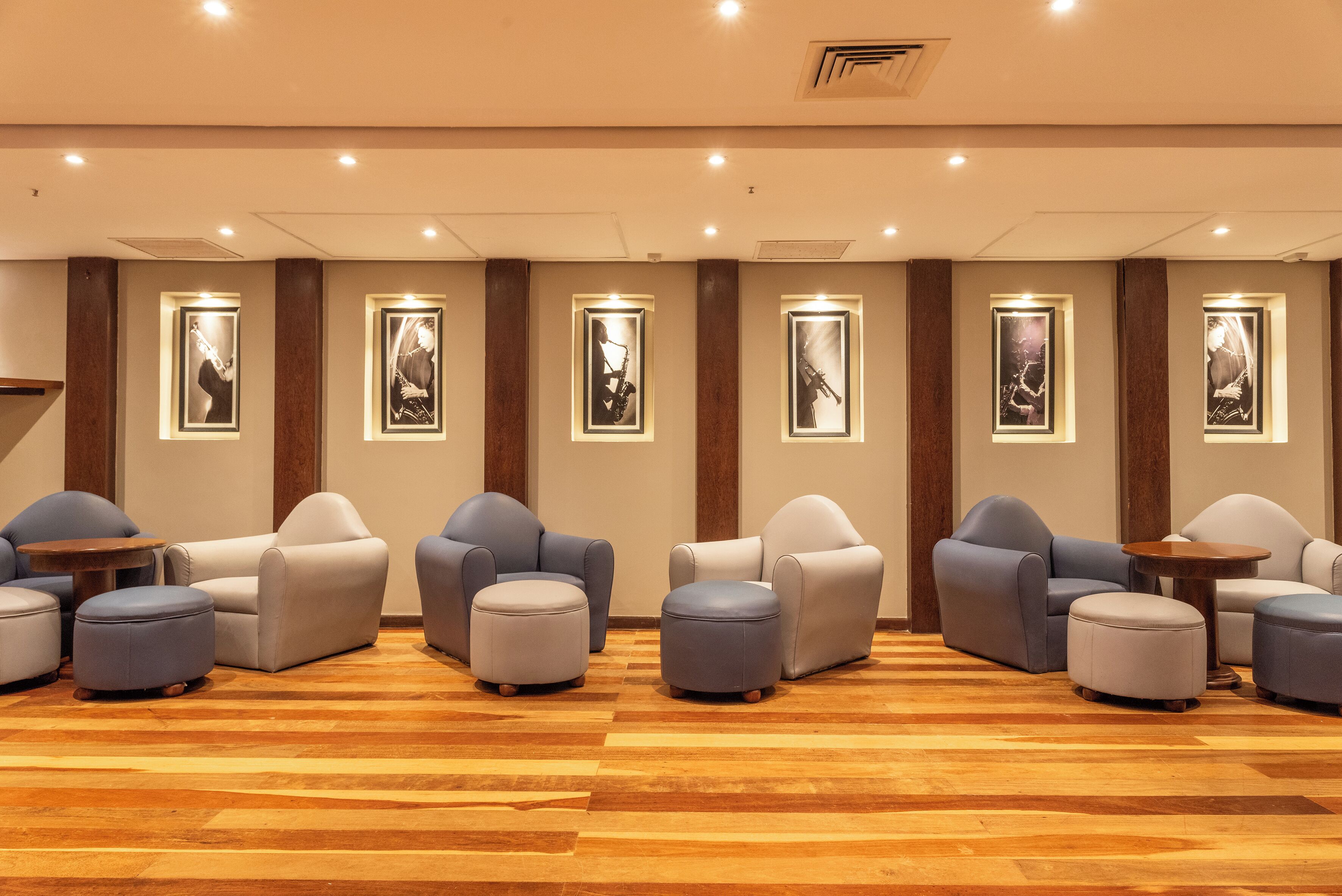 Um hall de hotel com piso de madeira, várias áreas de estar com sofás e pufes, e obras de arte emolduradas nas paredes.