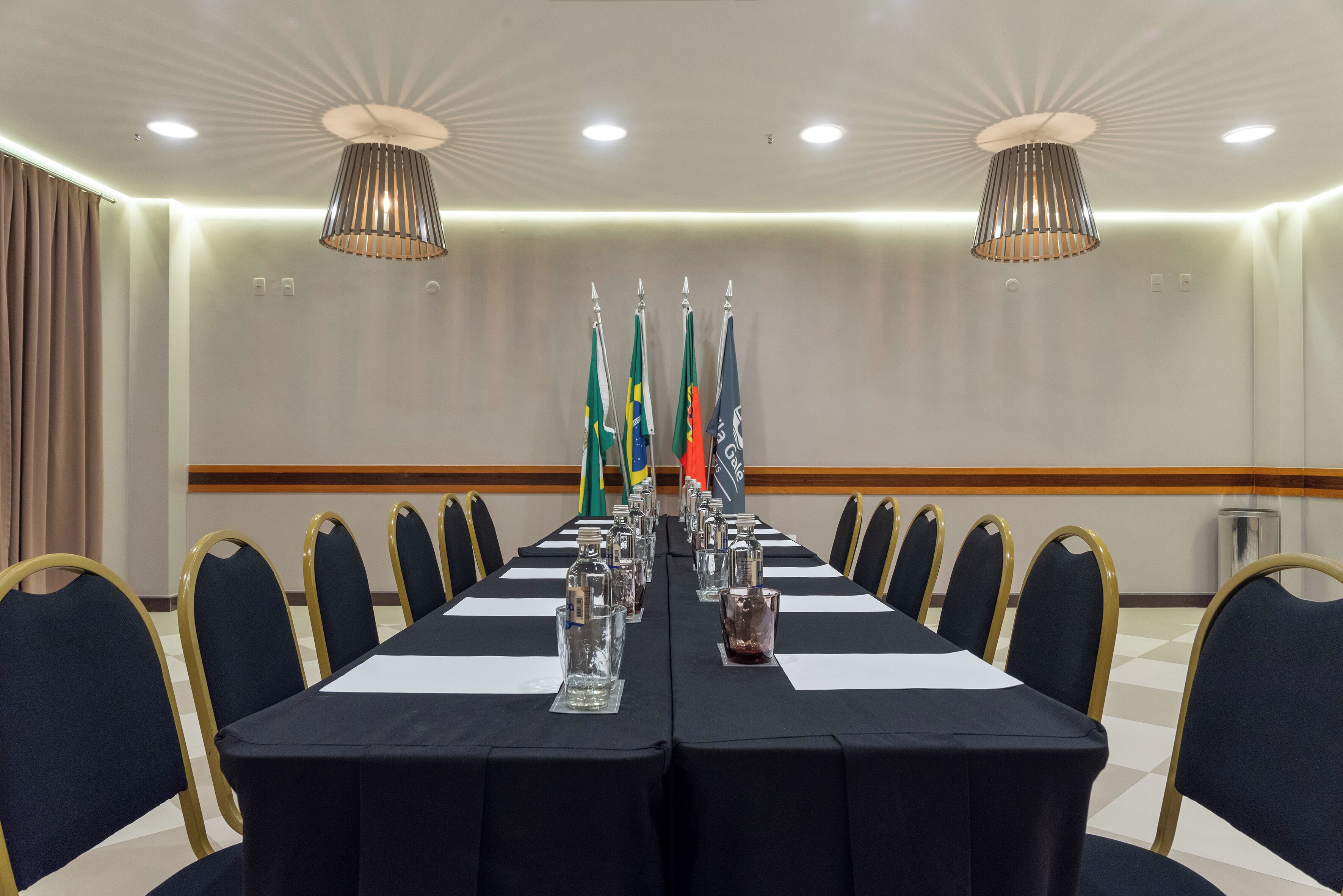 A conference room with a long table, chairs, flags, and a chandelier.