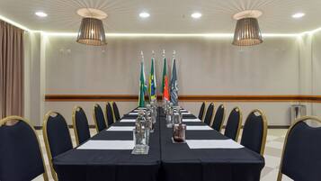 A conference room with a long table, chairs, flags, and a chandelier.
