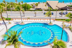 A swimming pool with a circular design, surrounded by palm trees and lounge chairs, with a view of the beach and hotel buildings in the background. - Vila Gale Fortaleza (Fortaleza)