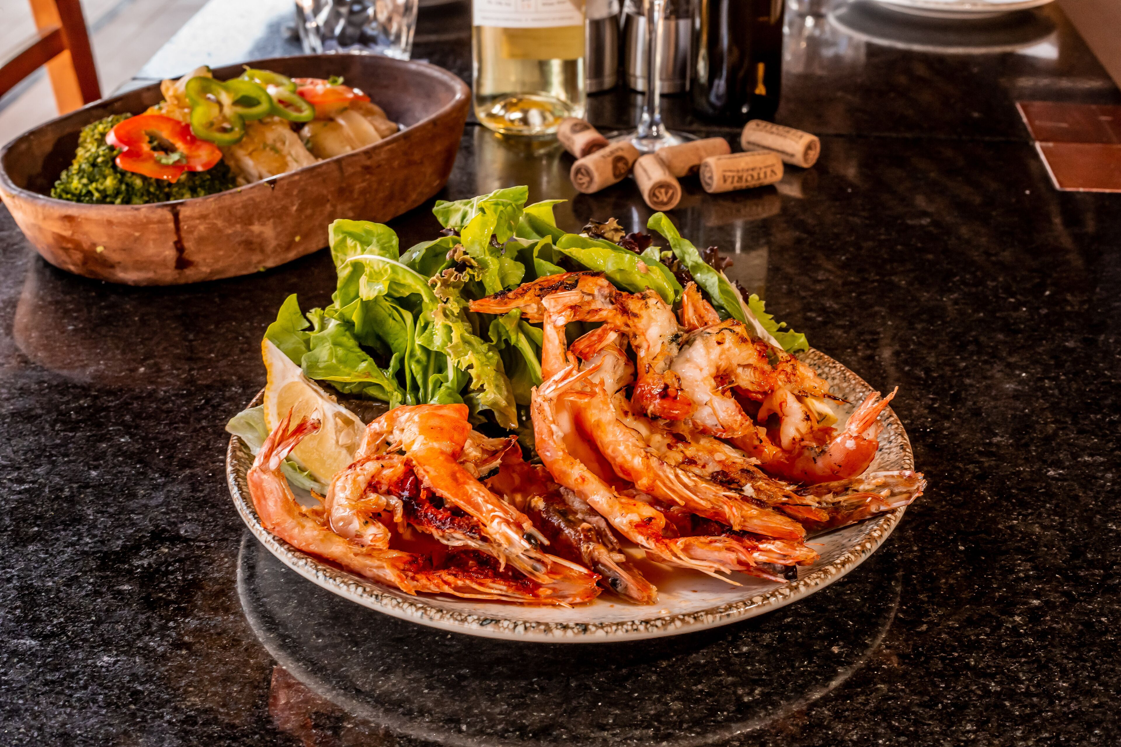 Una mesa de comedor con un plato de camarones cocidos y un bol de ensalada.