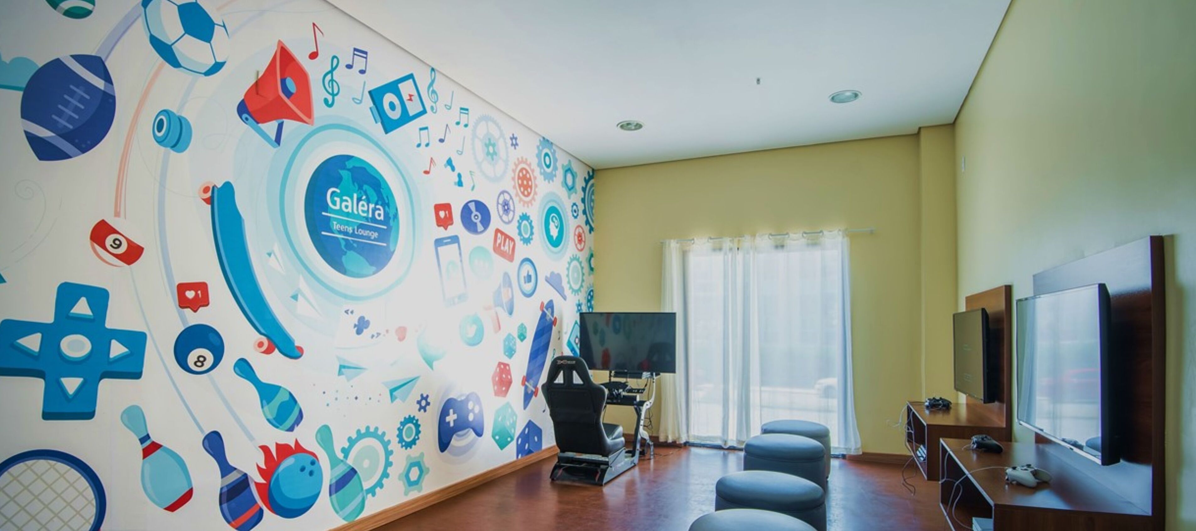A room with a wall mural featuring various icons, a gaming chair, a large TV, and a gaming console.