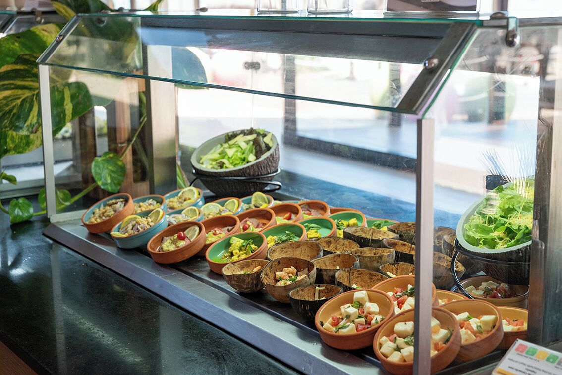 Buffet com diversos pratos em tigelas, alguns com ingredientes visíveis como vegetais e queijo.