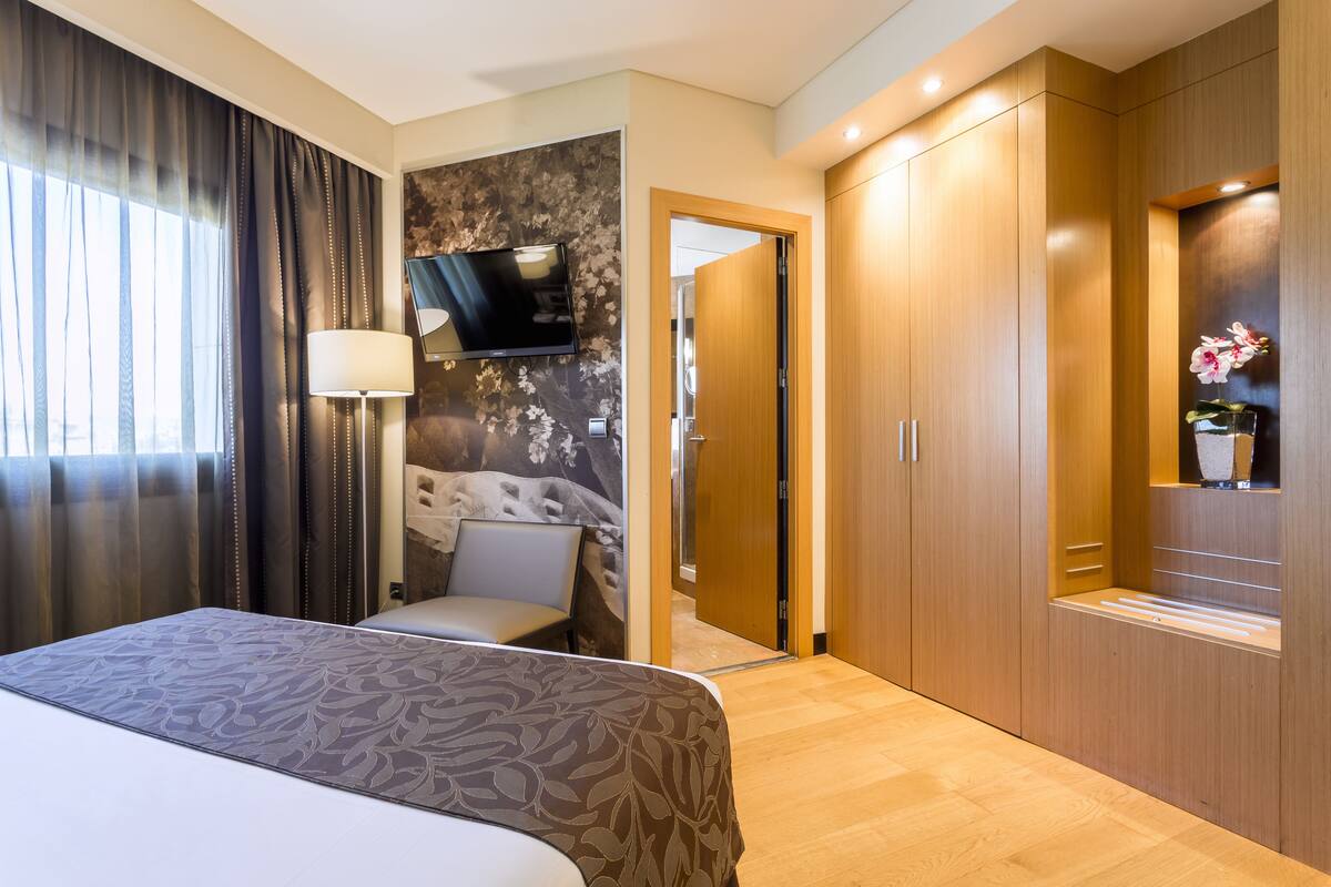 Une chambre d’hôtel équipée d’un lit, d’un bureau, d’une chaise, d’un téléviseur fixé au mur et d’une armoire.