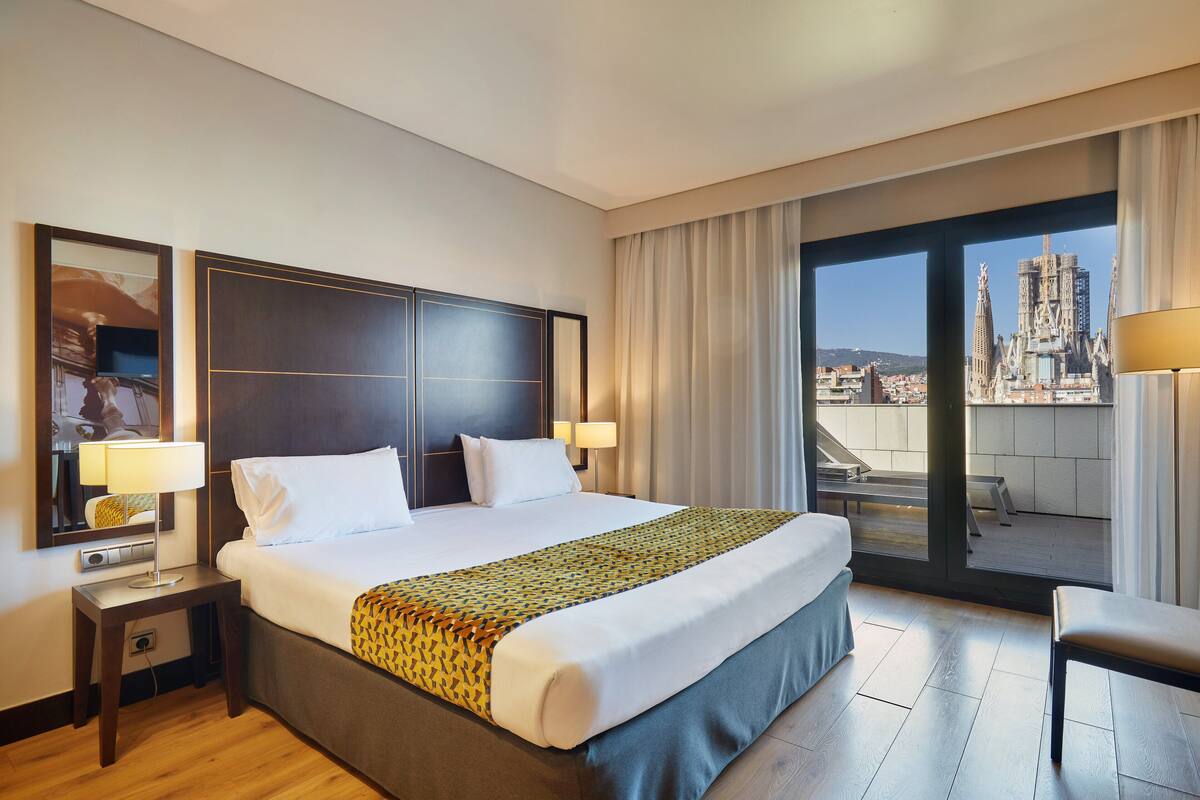 Une chambre d’hôtel avec un grand lit, deux tables de chevet, une chaise et un balcon offrant une vue sur la ville.