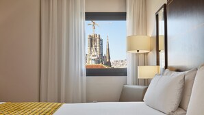 A hotel room with a large bed, two bedside lamps, a view of a cityscape with a tall building, and a window with curtains. - Eurostars Monumental (Barcelona)