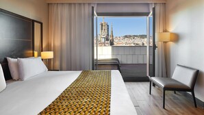 A hotel room with a large bed, a bench, and a view of a cityscape. - Eurostars Monumental (Barcelona)