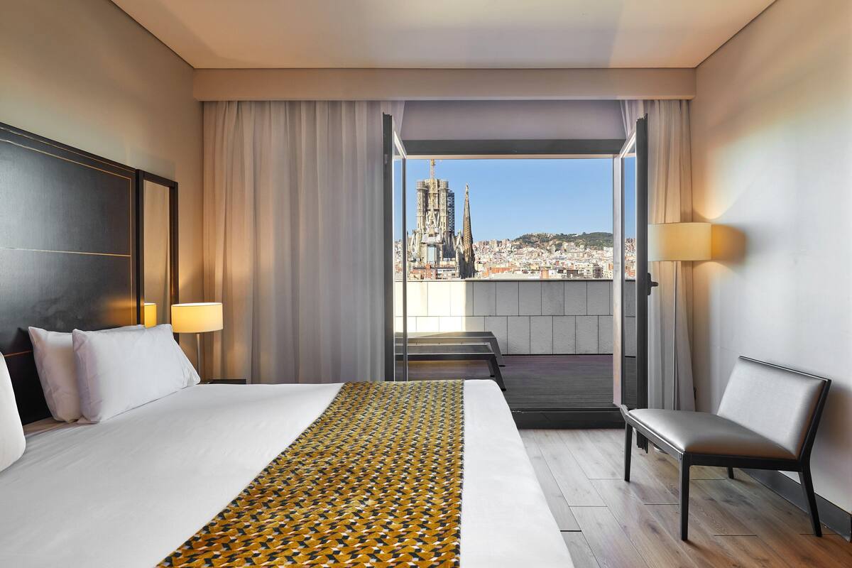 Une chambre d’hôtel avec un grand lit, un banc et une vue sur le paysage urbain.