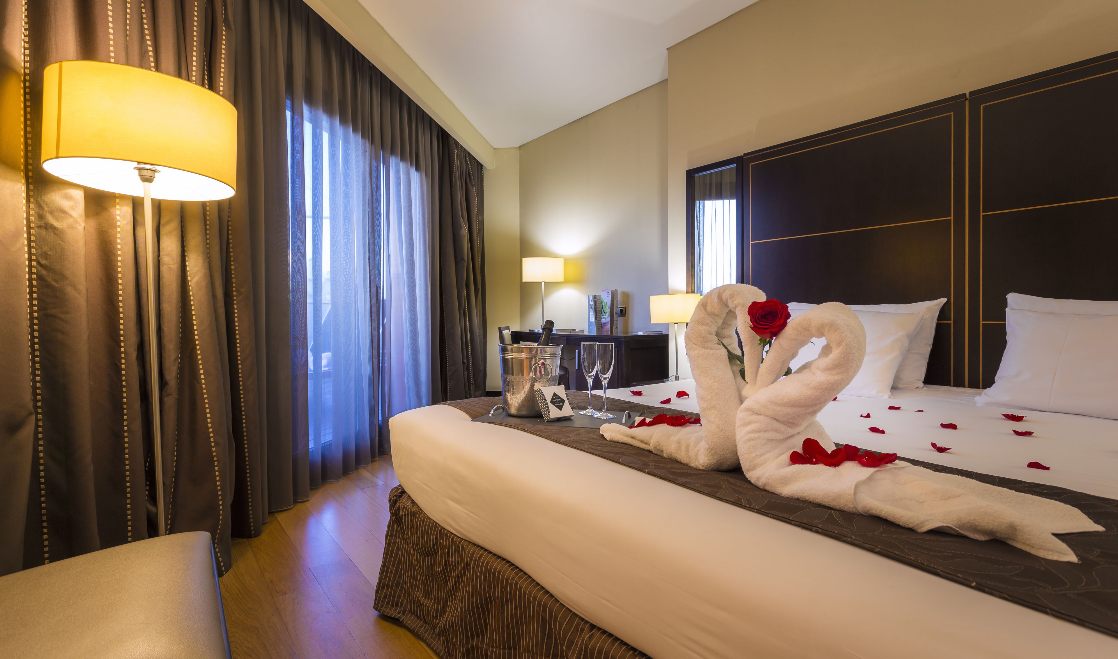 Une chambre d’hôtel avec un grand lit, un bureau, une lampe et des rideaux.