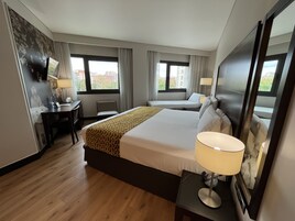 A hotel room with a large bed, a desk, a chair, and two windows.