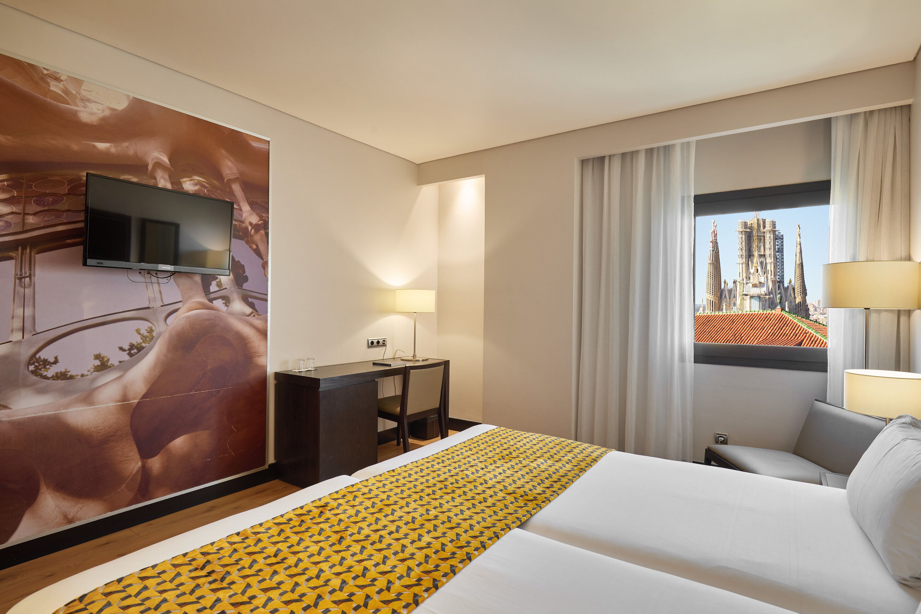 Habitación de hotel con cama, escritorio, televisión y ventana con vista a la ciudad.