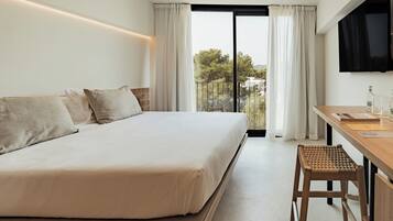 A hotel room with a large bed, a desk with a chair, a TV mounted on the wall, and a balcony with curtains.