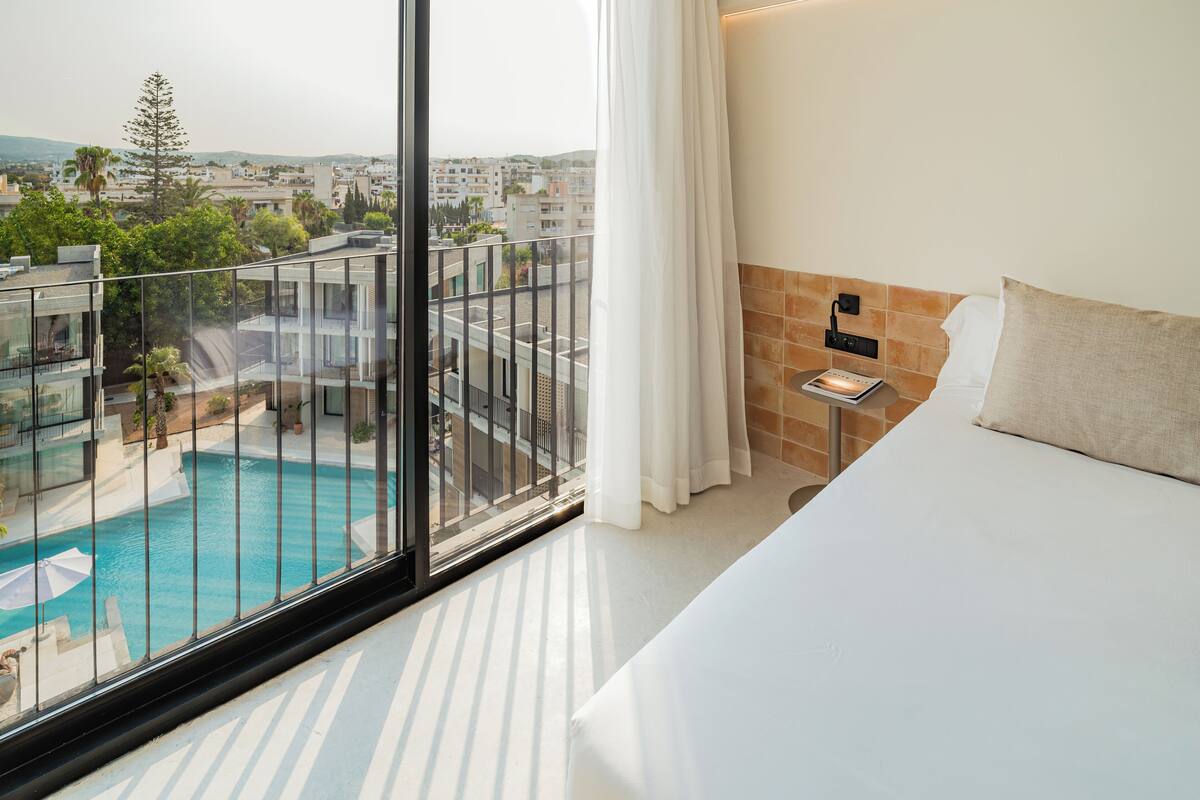 A hotel room with a large window overlooking a swimming pool and a cityscape.