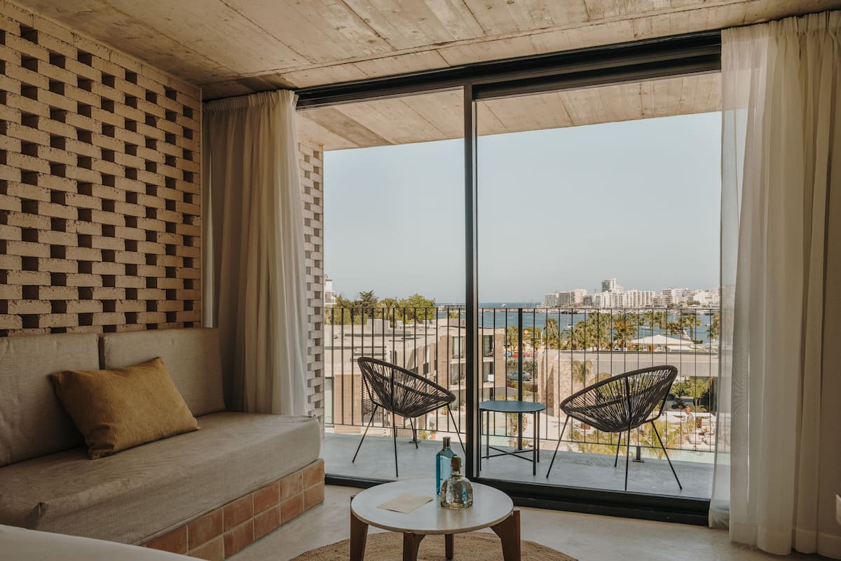 A balcony with a view of the city and the sea, a sofa, two chairs, and a small table.