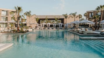 A swimming pool with lounge chairs and umbrellas, surrounded by palm trees and modern buildings.