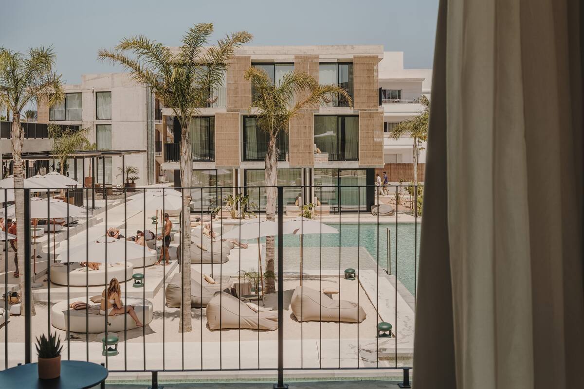 A poolside area with lounge chairs and umbrellas, a modern building in the background, and a view through a metal railing.