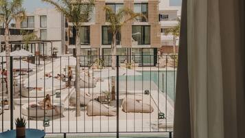 A poolside area with lounge chairs and umbrellas, a modern building in the background, and a view through a metal railing.