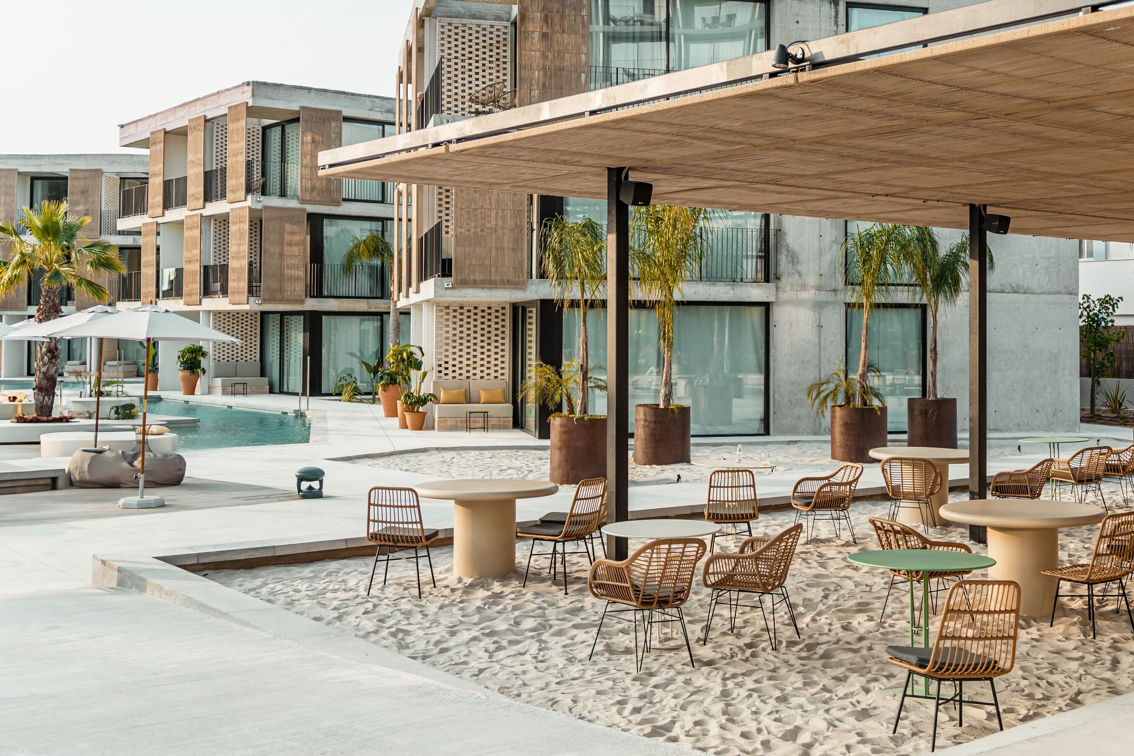 Un espace extérieur moderne aménagé avec des tables et des chaises, une piscine et un bâtiment doté de balcons et de grandes fenêtres.