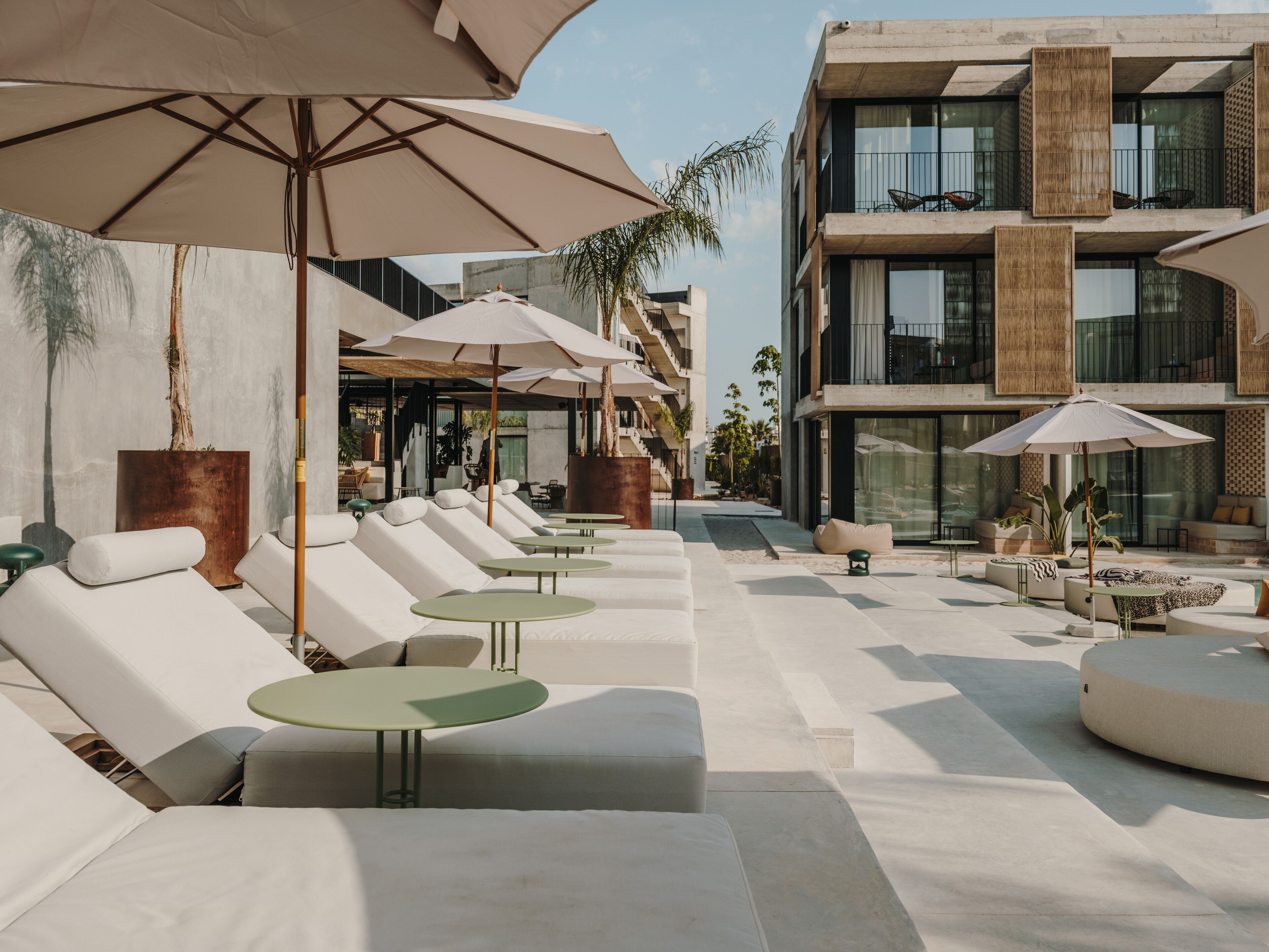 A modern outdoor lounge area with white lounge chairs and green tables, shaded by large umbrellas.