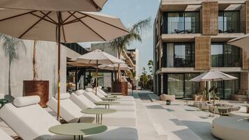 A modern outdoor lounge area with white lounge chairs and green tables, shaded by large umbrellas.