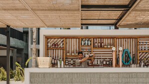 A bar area with a bartender preparing drinks, shelves of liquor bottles, and a decorative item on the wall. - Bonito Ibiza by NCalma Hotels (Sant Antoni de Portmany)