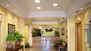 Vestíbulo de hotel con piso de mármol, mostrador de recepción de madera, plantas en macetas y una zona de recepción con mostrador y sillones.