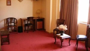 Habitación de hotel con alfombra roja, televisor montado en la pared, una mesita de noche con lámpara y dos sillas.