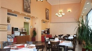 Un restaurante con varias mesas y sillas, una zona de cocina y una planta grande en maceta.