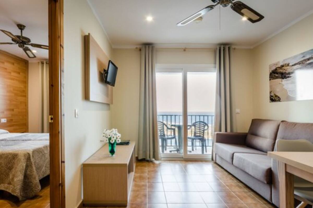 Habitación de hotel con cama, sofá, una mesita, televisor, balcón con vistas y ventilador de techo.