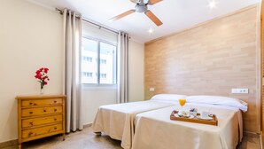 Hotelkamer met twee bedden, een houten dressoir, een raam met gordijnen, een plafondventilator en een ontbijttafel op het bed.