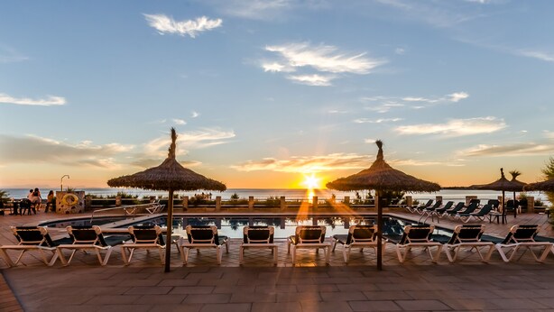 Een zwembadterras met ligbedden en parasols, met uitzicht op een waterpartij in de zonsondergang.
