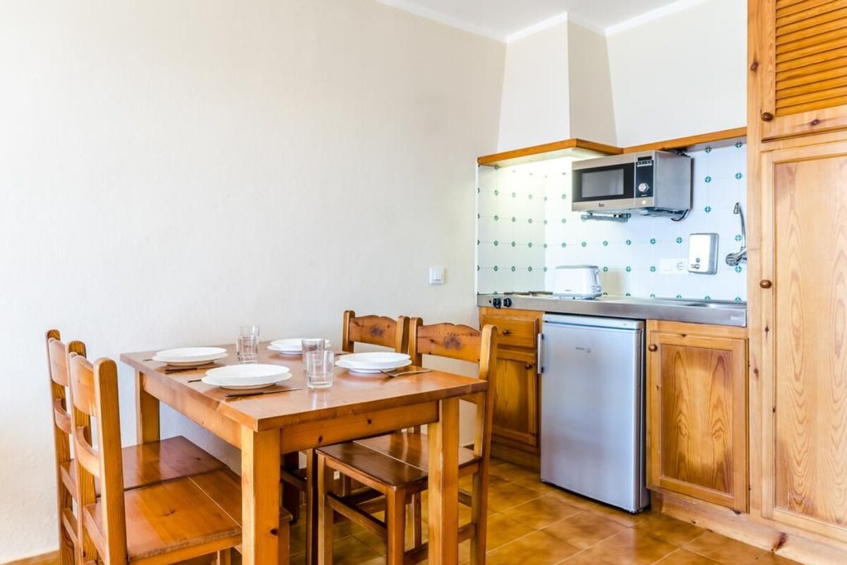 Una cocina compacta con armarios de madera, un microondas y un refrigerador pequeño.