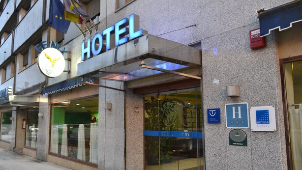 Entrada de un hotel con un cartel llamativo que dice 'HOTEL', un símbolo de accesibilidad para sillas de ruedas y un letrero de seguridad contra incendios.