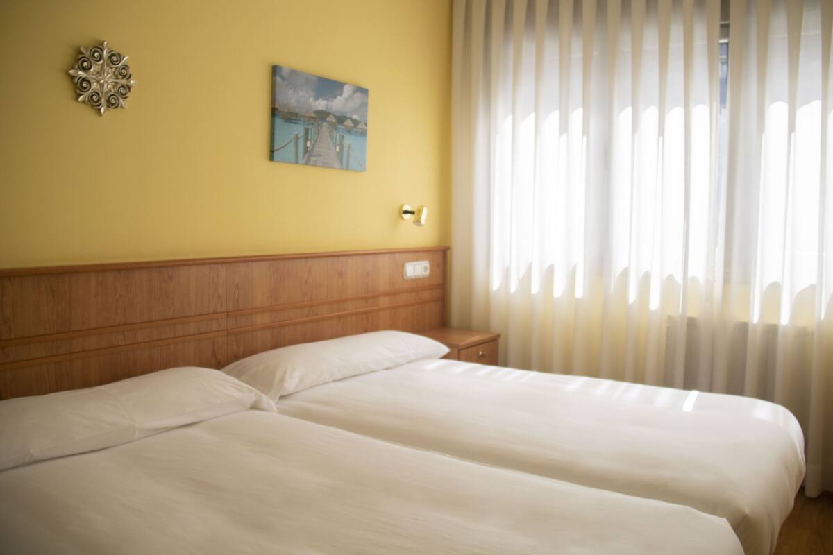 Un lit double avec une tête de lit en bois, une table de chevet, une lampe fixée au mur et un tableau.