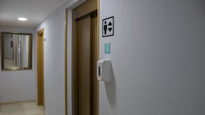Un pasillo con una puerta, dispensador de gel antibacterial y señalización de baño inclusivo.
