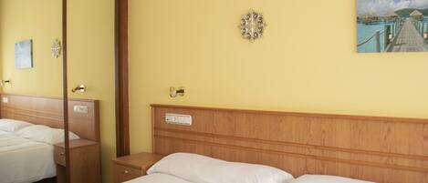 A hotel room with a wooden headboard, a bed with white linens, a bedside table, a nightstand, a mirror, and a wall-mounted decorative item.