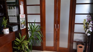 Un área de recepción con un mostrador de madera, una planta en maceta, un tablón de anuncios y una puerta de vidrio con paneles satinados.